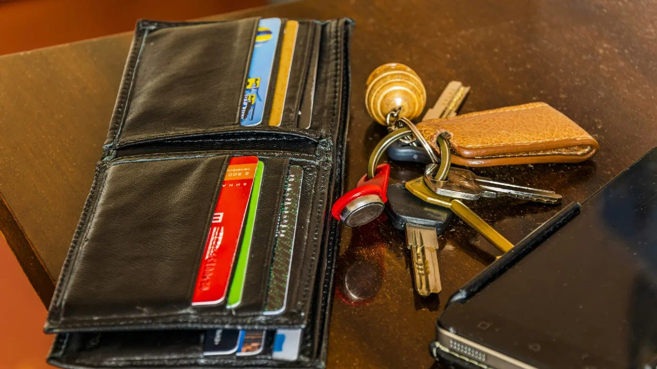 A wallet, a phone and a set of keys lying on a dark wooden table