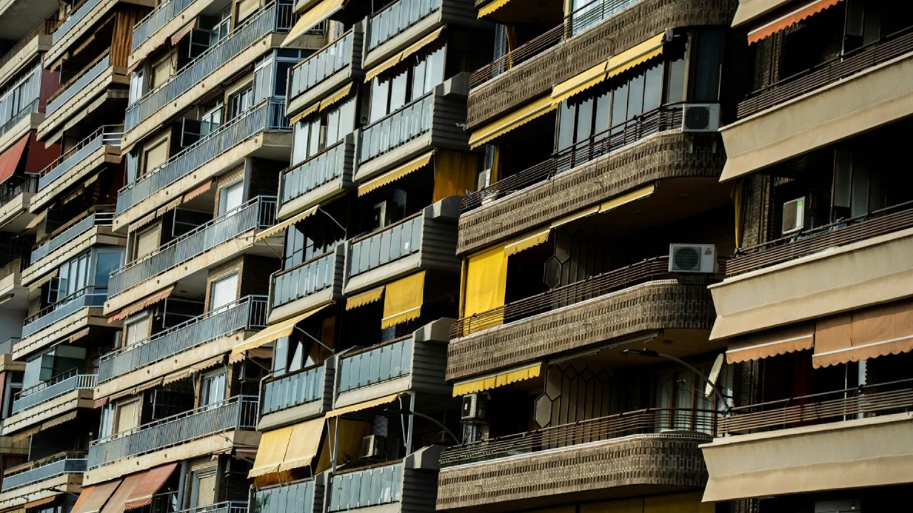 Rows of apartment balconies with awnings and air-conditioning units on a sunlit building front