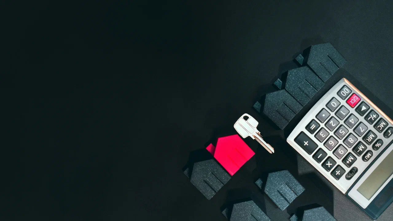 A silver door key and a small red house model beside a calculator on a black surface
